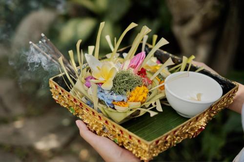 a person holding a plate of flowers and a bowl at Uddhara Ubud Villa in Ubud