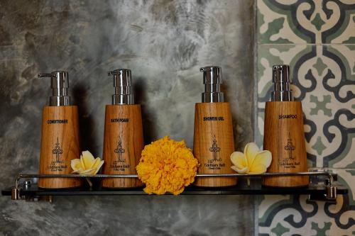 a shelf with four shampoo bottles and flowers on it at Uddhara Ubud Villa in Ubud