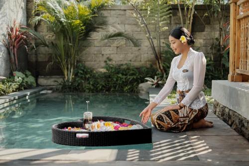 a woman kneeling next to a pool with a table of candy at Uddhara Ubud Villa in Ubud