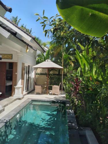 a swimming pool in front of a house with an umbrella at Lovina Garden Retreat in Lovina