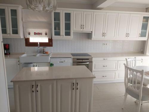 a white kitchen with white cabinets and a table at Şifne yalı'da 4 oda 9kisi yatak kapasite manzaralı in Cesme