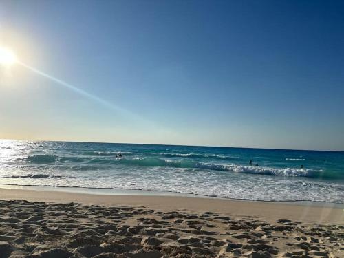 a beach with people surfing in the ocean at Panoramic see view apartment in North Coast الساحل الشمالي in Alexandria