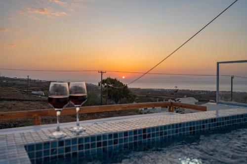 two glasses of wine sitting on a table with the sunset at Theophrasti Suites in Foinikiá