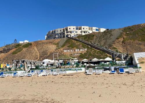 a beach with chairs and a hotel on a hill at Appartement bord de mer in Jbila