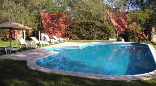 una piscina azul con sillas y sombrilla en La Campiña Cabañas en Santa Rosa de Calamuchita