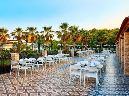 a row of tables and chairs on a patio with palm trees at Mövenpick Resort Antalya Tekirova - Ultra All Inclusive in Tekirova