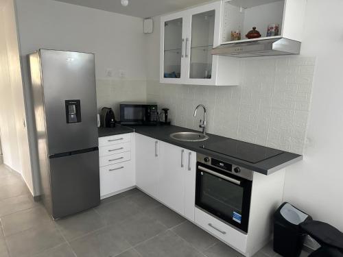 une cuisine avec des armoires blanches et un réfrigérateur en acier inoxydable dans l'établissement Appartement - Paris, Disney, Parc des expos, Aéroport CDG, RER B, à Sevran