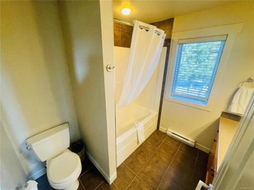 a bathroom with a toilet and a shower and a window at Sheringham Townhouse - Sooke in Sooke