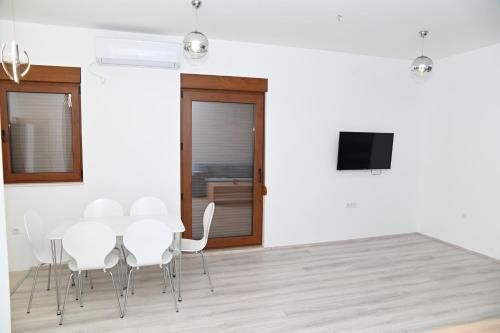 a dining room with white chairs and a flat screen tv at Villa Panorama - autumn luxury villa - heated pool and jacuzzi in Ivanica