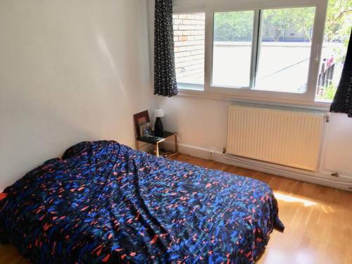 une chambre avec un lit avec une couette colorée et une fenêtre dans l'établissement Charmant Appartement Proche des Buttes-Chaumont, à Paris