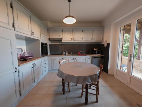 une cuisine avec des armoires blanches et une table avec des chaises dans l'établissement Grande maison en Périgord à 10 mn de Sarlat, à Marquay