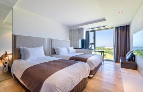 two beds in a hotel room with a large window at Sungsan Marina Hotel in Seogwipo