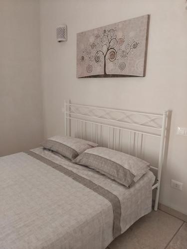 Una cama en una habitación blanca con un cuadro de un árbol en la pared. en Casa Vacanze Livia Maria, en San Cassiano