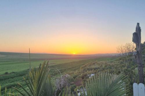 a sunset over a field with the sun setting in the distance at וילה במושב בנוף מושלם כל השנה in Moledet