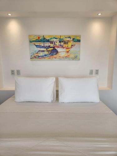 two white pillows on a bed with a painting on the wall at Pousada Dreamland Buzios in Búzios