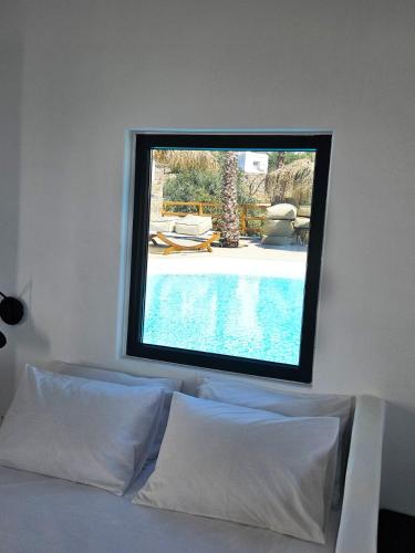 a window above a bed with a swimming pool at ELLI TROPiCAL LUXURY SUITES SUNSET-INFINITY POOL- SEA SIDE-NEAR CENTER PARKING in Mikonos