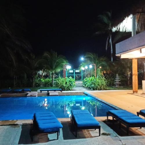 a swimming pool at night with blue cushioned chairs around it at QUINTA DIAMANTE villas&hotel in Barra Vieja