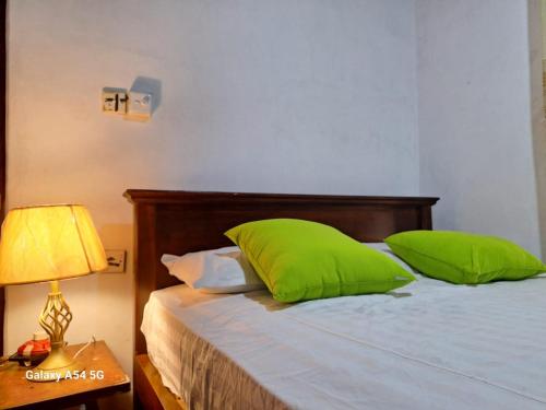 a bedroom with a bed with green pillows and a lamp at Ajanee HomeStay in Tangalle