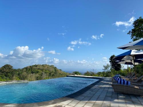 a swimming pool with chairs and an umbrella at Kubuhill Sunset Bungalow in Nusa Penida