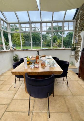 une salle à manger avec une table, des chaises et des fenêtres dans l'établissement La Paix, Chalet de charme dans le Bocage Normand, à Condé-sur-Noireau