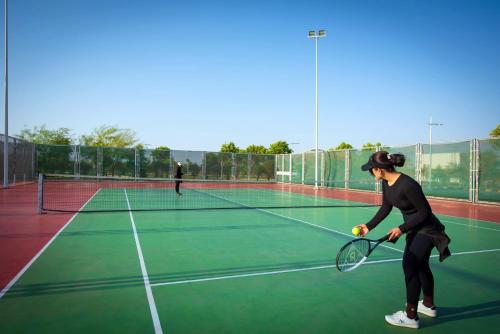 a woman holding a tennis ball and racket on a tennis court at Grand Millennium Tabuk in Tabuk