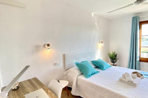 a bedroom with a bed with blue pillows and a table at Apartament Sa Farola - AC, WiFi , Pool, Beach in Cala en Blanes