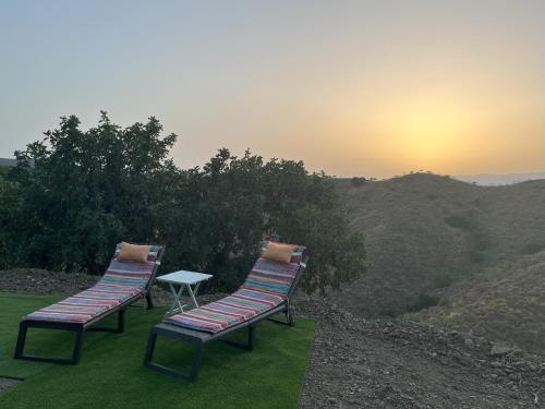 two chairs and a table on a hill with the sunset at Guesthouse Un Poco Mas in Canillas de Aceituno