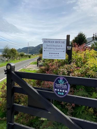a sign on a fence next to a road at Rowan House B&B Rooms & A Self Catering Apartment in Lochgoilhead