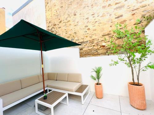 a patio with a couch and a table with an umbrella at 30 m plage Le Roulis classée 3 étoiles, jolie maison entièrement rénovée en 2024 in Les Sables-dʼOlonne