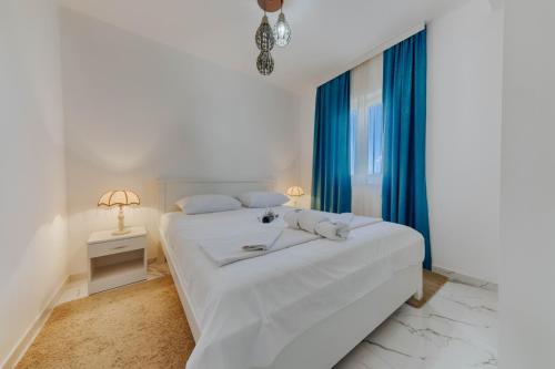 a white bedroom with a large bed with blue curtains at Morski plamen in Kruče