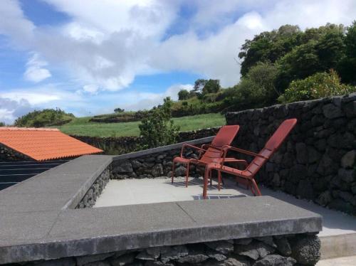 two red chairs sitting next to a stone wall at Casa do Norte in Prainha de Cima