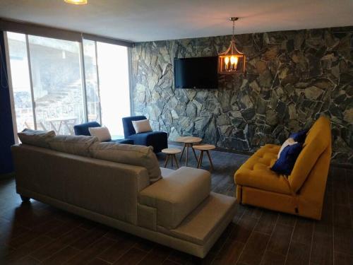 ein Wohnzimmer mit einem Sofa, Stühlen und einer Steinmauer in der Unterkunft Hermoso Depto en Club Burgos Bugambilias Temixco in Temixco