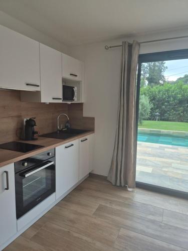 a kitchen with white cabinets and a large window at Rez de villa avec piscine privée, wifi, jardin clôturé in Penta-di-Casinca