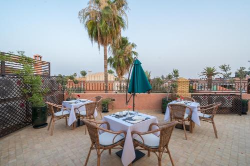 a patio with tables and a green umbrella and palm trees at Riad Atlas Palace & SPA in Marrakech