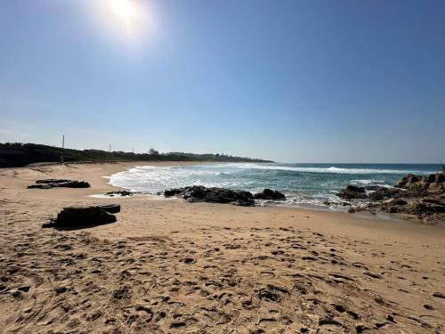 a sandy beach with rocks and the ocean at Tranquility - Banana Beach Club in Port Shepstone