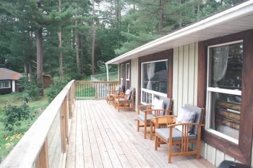 une terrasse en bois avec des chaises et des tables sur une maison dans l'établissement Escape to Corry Lake Cottage, à Chalk River