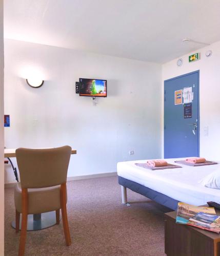 Cette chambre comprend un lit, une chaise et une télévision murale. dans l'établissement Hotel La Voile Bleue, à La Richardais