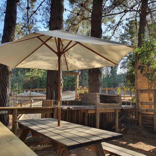 a wooden picnic table with an umbrella on it at Glamping Puertecillo Surf & Camp in Puertecillo