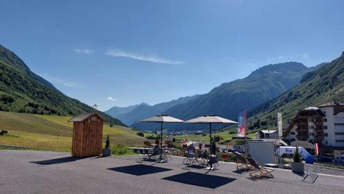 a patio with tables and umbrellas with mountains in the background at Hotel Garni Bel-Ami in Galtür