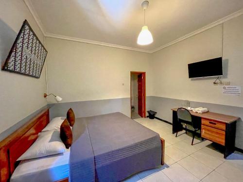a bedroom with a bed and a desk and a television at Wisma Anugerah Redpartner Near Masjid Zayed Solo in Bonorejo