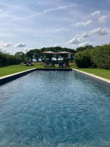 une piscine avec chaises et parasols dans une cour dans l'établissement Chambres d'hôtes La Massonnière avec grand jardin - idéal familles, groupes et séjour nature - Sarthe, à Saint-Christophe-en-Champagne