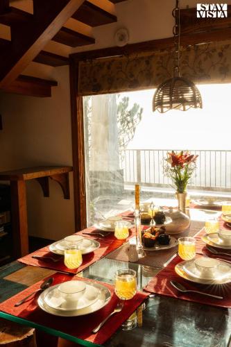 a table with plates of food on it with a window at StayVista at The Rustic Retreat - 4BHK Valley View villa with Lawn, Bonfire in Kasauli