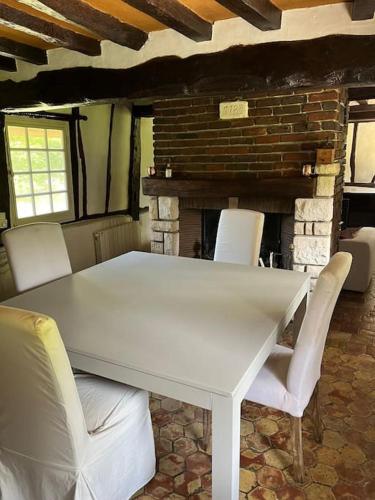 - une table et des chaises blanches dans une pièce avec cheminée dans l'établissement La belle chaumière, à Illeville-sur-Montfort