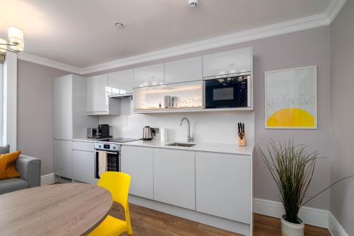 a kitchen with white cabinets and a table and a yellow chair at 37 Doughty Street - Urban Apartments in London