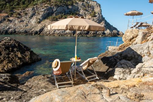 a pair of chairs and an umbrella on a beach at Boutique Hotel Torre Di Cala Piccola in Porto Santo Stefano
