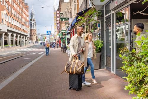 a man and woman walking down a street with a suitcase at Albus Hotel Amsterdam City Centre in Amsterdam