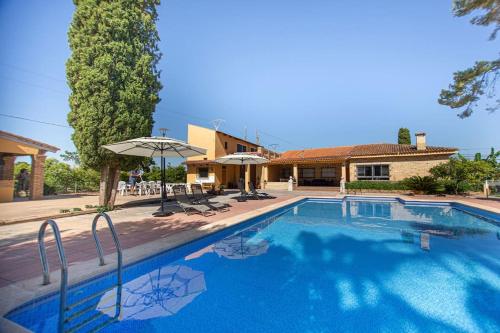 a swimming pool with chairs and umbrellas next to a house at Villa con piscina y barbacoa para 13 personas cerca del metro in Valencia