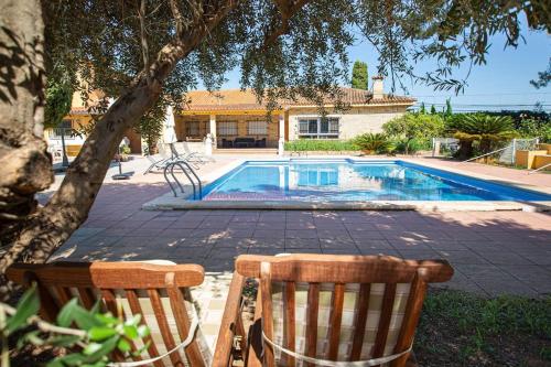 a swimming pool with two chairs in front of a house at Villa con piscina y barbacoa para 13 personas cerca del metro in Valencia