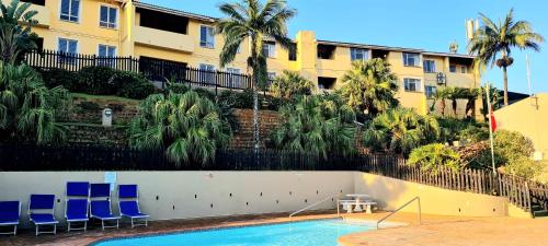 a swimming pool in front of a building with blue chairs at Chaka's Rock Beach Chalet 54 in Ballito