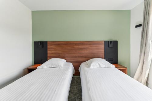 two beds in a small room with a headboard at Hôtel Akena Pierrelaye in Pierrelaye